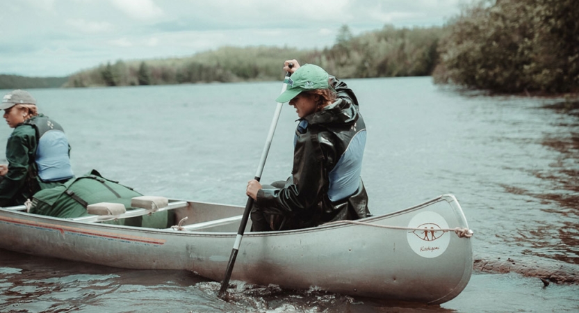 Two people wearing life jackets navigate a canoe on calm water